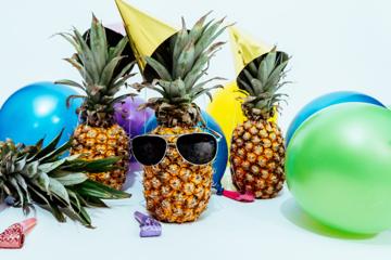 Multiple balloons in different colors, pineapples wearing party hats, and sunglasses.